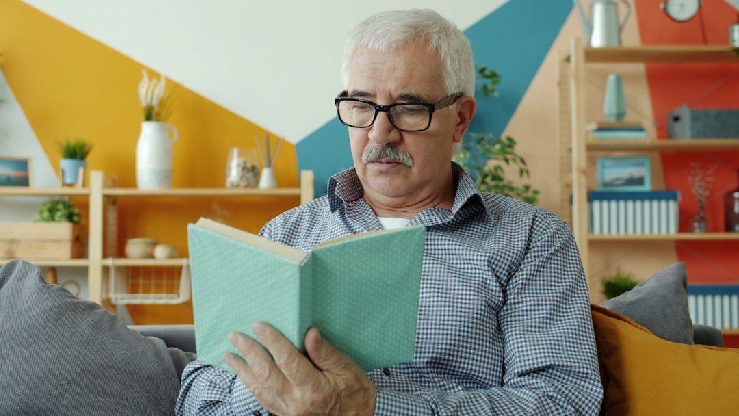 Older Croatian man with glasses reading a book at home